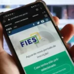 Mãos que seguram um celular mostrando o site do Fies